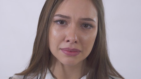 Closeup of young woman crying on white background.