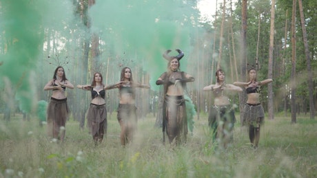 Costumed women belly dance in forest music video.