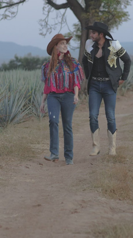Couple dressed as charros walking through a farm.