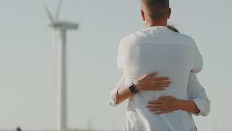 Couple embracing in the sunshine near a wind turbine.