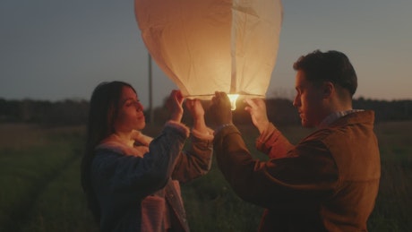 Couple holding a lantern in the countryside at sunset.