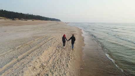 Couple holding hands walking along an empty beach.