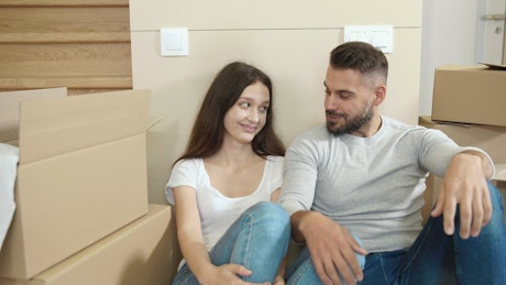 Couple in jeans cuddle among moving boxes.