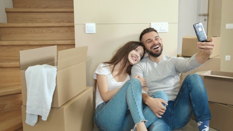 Couple in jeans take selfies in new apartment.