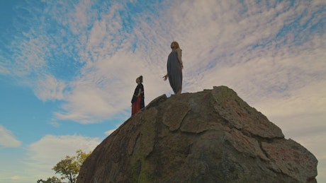 Couple of people meditating on top of a rock.
