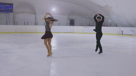Couple of skaters performing figure skating routine.