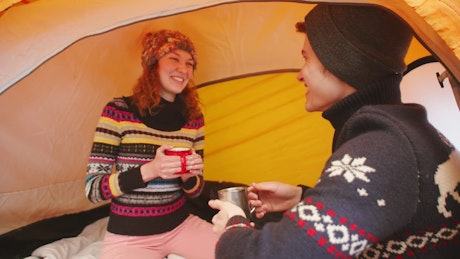 Couple sharing a laugh in a tent while camping in the snow.