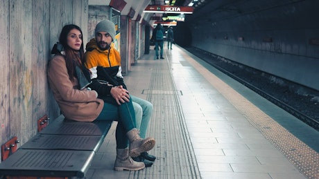 Couple sitting on a bench waiting for the next train to arrive.