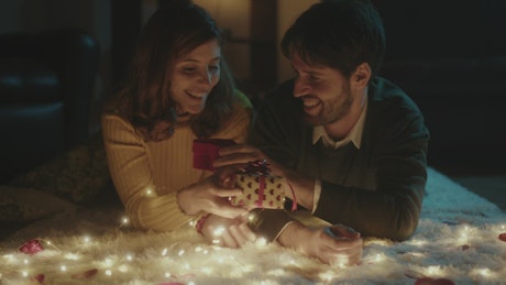 Couple surrounded by lights exchanging Valentine's Day gifts.