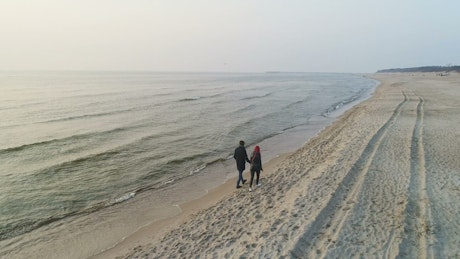 Couple walk along shore together.