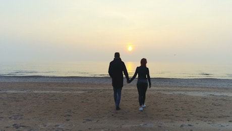 Couple walking on a beach towards the water.