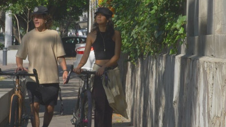Couple walking with bicycles on the sidewalk.
