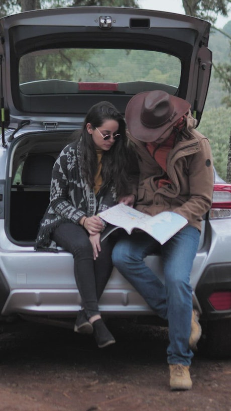 Couple watching a map in the trunk of a car.
