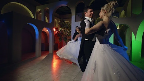 Couples dressed in formal attire waltzing at a ball.