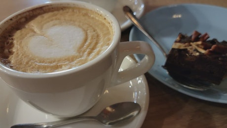 Cup of barista-made coffee and a slice of chocolate cake in a cafe.