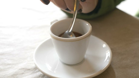 Cup of espresso being stirred with a spoon.