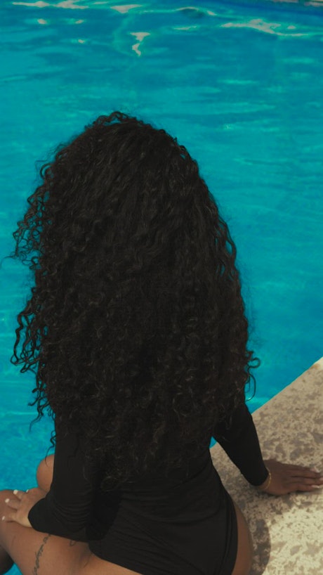Curly haired girl at a pool wearing sunglasses.