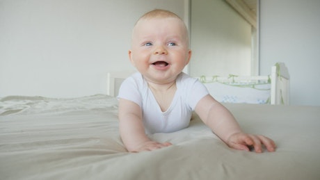 Cute laughing baby rolls over on bed.