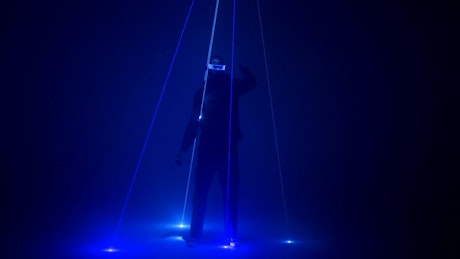 Dancer in electronic mask stands under laser lights.