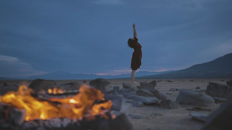 Deserted plain with a campfire and a woman practicing yoga.