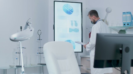 Doctor looks at screen showing DNA and brain models.