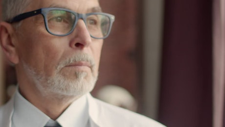 Doctor wearing glasses staring intensely out a window.