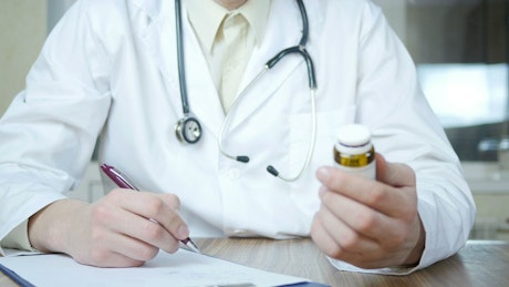 Doctor writing a prescription holding a medicine container.