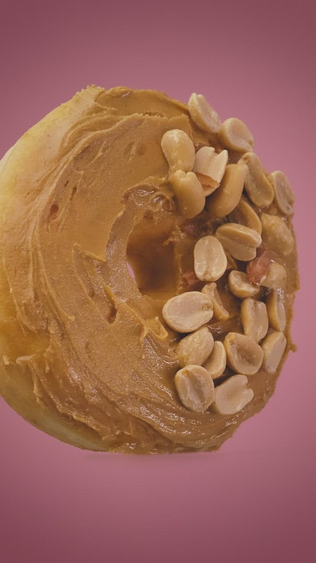 Donut with peanut butter and peanuts on a pink background.