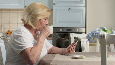 Elderly woman having a cup of tea while on the phone.
