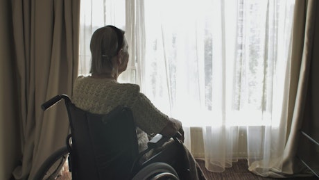 Elderly woman in wheelchair looking out the window.