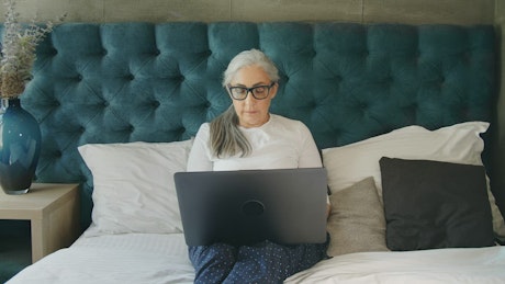 Elderly woman on laptop in blue bedroom