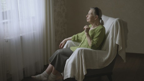Elderly woman sitting in a chair staring out the window.