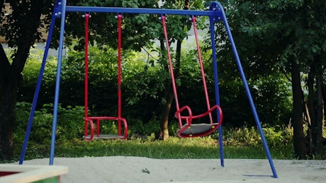 Empty swing set moving on its own in a playground.