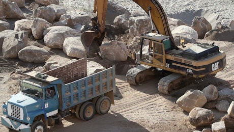 Excavation crane lifts a rock into a truck