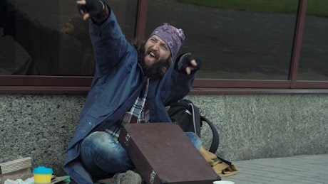 Excited happy homeless is drumming on a briefcase.