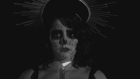 Face of a catrina blowing out a candle in the dark.