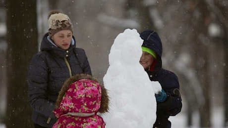 Family builds a snowman in the snow.