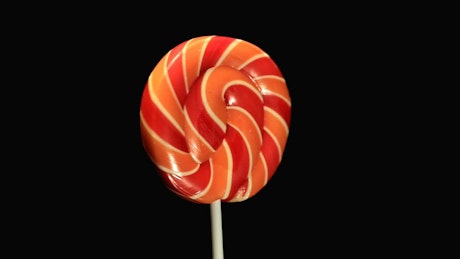 Fast spinning orange and red lollipop against a black background.