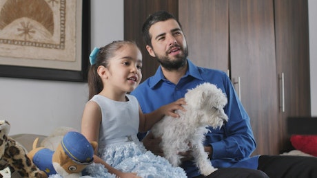 Father and daughter together watching television with their little dog.