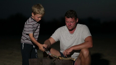 Father and son lighting a campfire at night