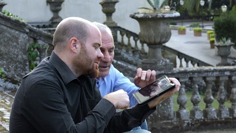 Father and son sit on steps outside using a tablet.