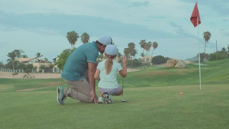 Father teaching daughter to play golf.