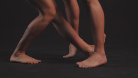 Feet of a pair of women dancing on a dark platform.