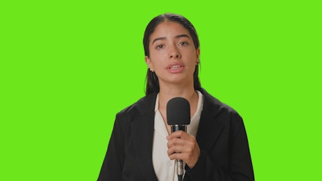 Female reporter reporting with microphone in hand on a chroma green background.