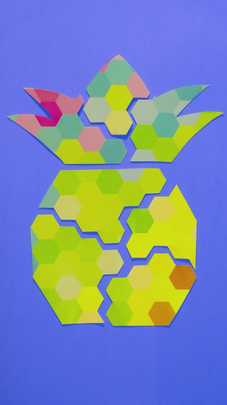 Figure of a pineapple made with pieces of paper on a blue background.