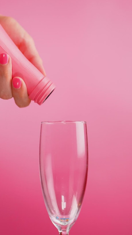 Filling a glass cup with small sweets on a pink background.