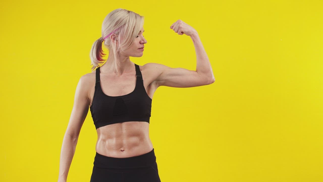Fit woman flexing her bicep against a yellow background - Free