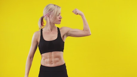 Fit woman flexing her bicep against a yellow background.