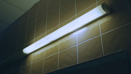Fluorescent bar light illuminates against tiles.