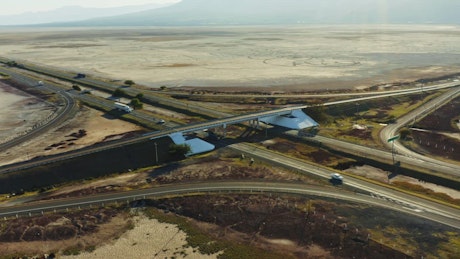 Flying over a highway overpass with a dry lake and mountains in the distance.